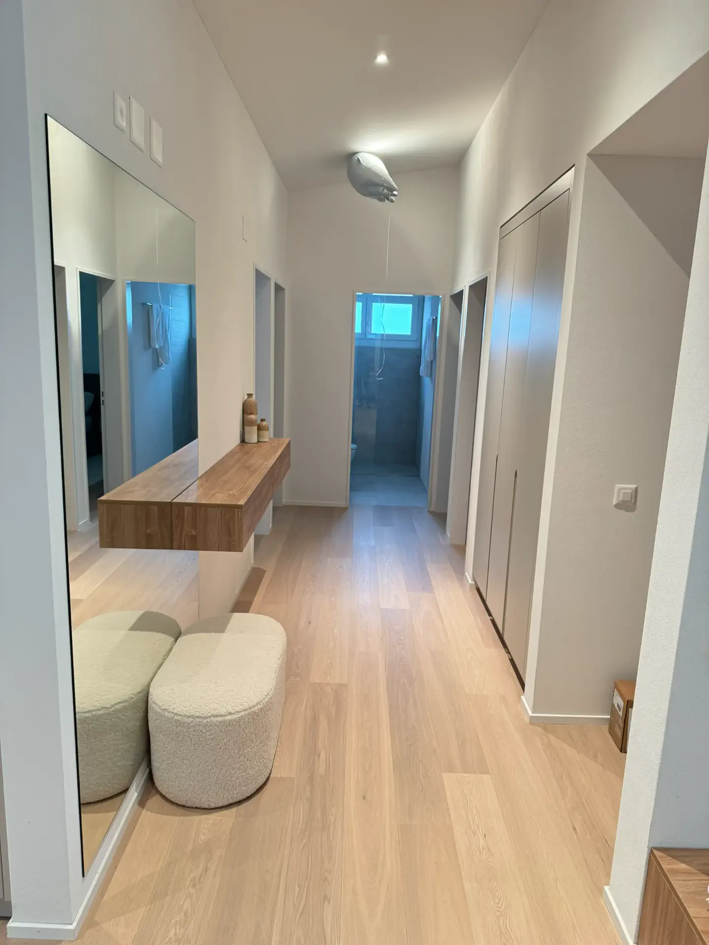 Heller Eingangsbereich mit Holzkonsole, großem Spiegel, Sitzhocker und Einbauschrank