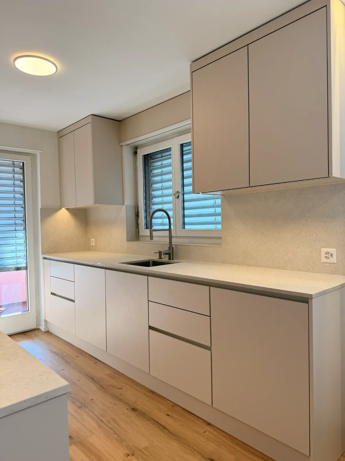 Grifflose maßgefertigte Küche in Sandbeige mit Arbeitsplatte und Rückwand in Natursteinoptik.