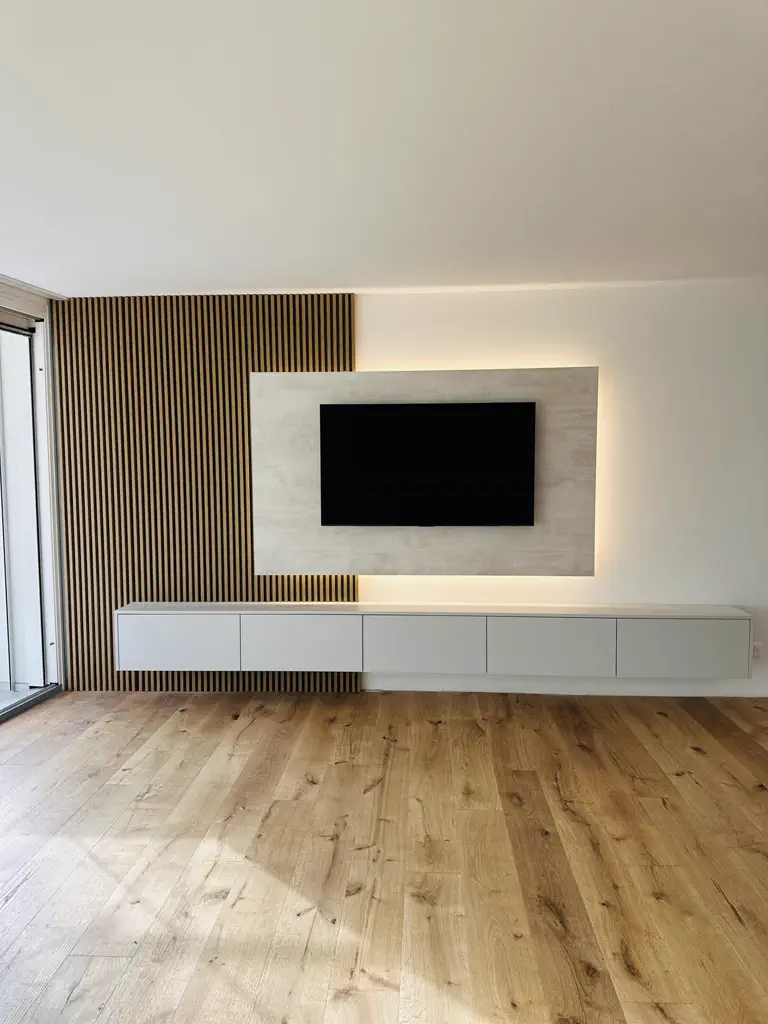 Moderne TV-Kommode in Weiß mit schwebender Konstruktion, kombiniert mit vertikalen Holzlamellen und beleuchtetem Wandpaneel